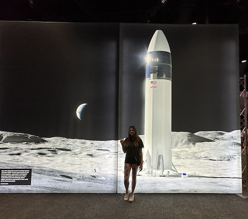 A woman standing in front of an image of a spaceship on the moon